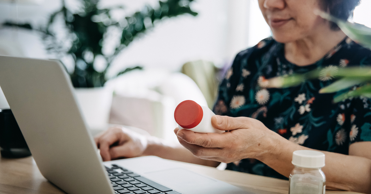Person holding a pill bottle while sitting and looking at a computer Person holding a pill bottle while sitting and looking at a computer