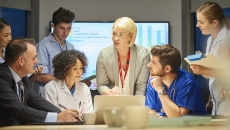 People sitting and standing around a table looking at a computer People sitting and standing around a table looking at a computer