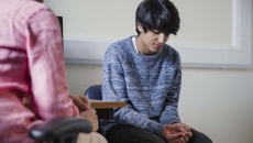 Two people sitting in a room, one with their head down Two people sitting in a room, one with their head down