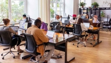 Numerous employees sitting at desks in a room with large windows Numerous employees sitting at desks in a room with large windows