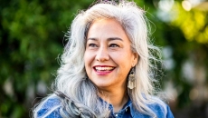 Person with long gray hair smiling while standing in front of trees Person with long gray hair smiling while standing in front of trees