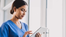 Nurse standing in a hallway holding a tablet Nurse standing in a hallway holding a tablet