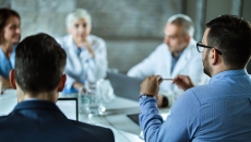 Five people sitting around a table speaking with each other Five people sitting around a table speaking with each other
