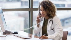 Healthcare provider on the phone while sitting at a desk with a computer on it Healthcare provider on the phone while sitting at a desk with a computer on it