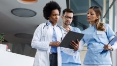 Three healthcare providers standing next to each other and looking at a tablet Three healthcare providers standing next to each other and looking at a tablet