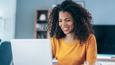 Person sitting in a house looking at a computer and smiling Person sitting in a house looking at a computer and smiling
