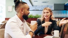 Two people sitting at a table while talking and looking at a computer Two people sitting at a table while talking and looking at a computer