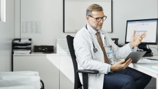 Doctor sitting in a chair at a desk while looking at a tablet Doctor sitting in a chair at a desk while looking at a tablet