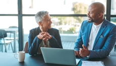 Two people sitting at a table with a laptop on it Two people sitting at a table with a laptop on it