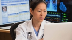 Healthcare professional sitting at a desk with many computers around them Healthcare professional sitting at a desk with many computers around them