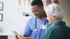 Healthcare provider standing next to a patient and holding a tablet that both individuals are looking at Healthcare provider standing next to a patient and holding a tablet that both individuals are looking at