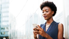 Person standing on the street while looking at their phone with a blurred city background Person standing on the street while looking at their phone with a blurred city background