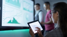 Person holds tablet while looking at information on a large screen Person holds tablet while looking at information on a large screen