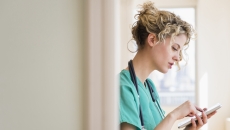 Nurse standing in a hallway while looking at a tablet Nurse standing in a hallway while looking at a tablet