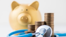 A piggy bank next to a pile of coins and a stethoscope. A piggy bank next to a pile of coins and a stethoscope.
