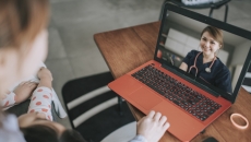 Two people sitting on a couch while looking at an orange and black computer and speaking with a virtual healthcare provider Two people sitting on a couch while looking at an orange and black computer and speaking with a virtual healthcare provider