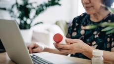 A close up of a woman holding a prescription bottle while using a laptop A close up of a woman holding a prescription bottle while using a laptop