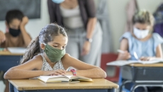 12 year old girl wearing a reusable, protective face mask in classroom while working on school work at her desk. 12 year old girl wearing a reusable, protective face mask in classroom while working on school work at her desk.