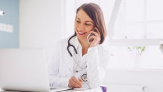 A doctor on the phone with a patient while checking their medical record on a laptop computer