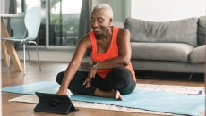 A person using a tablet while sitting on a yoga mat and preparing to exercise A person using a tablet while sitting on a yoga mat and preparing to exercise