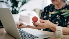 A woman holding a pill bottle using a laptop
