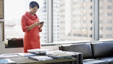 A woman standing at her desk looking down at her smartphone A woman standing at her desk looking down at her smartphone
