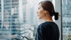 A woman holding a smartphone looking out a window. A woman holding a smartphone looking out a window.