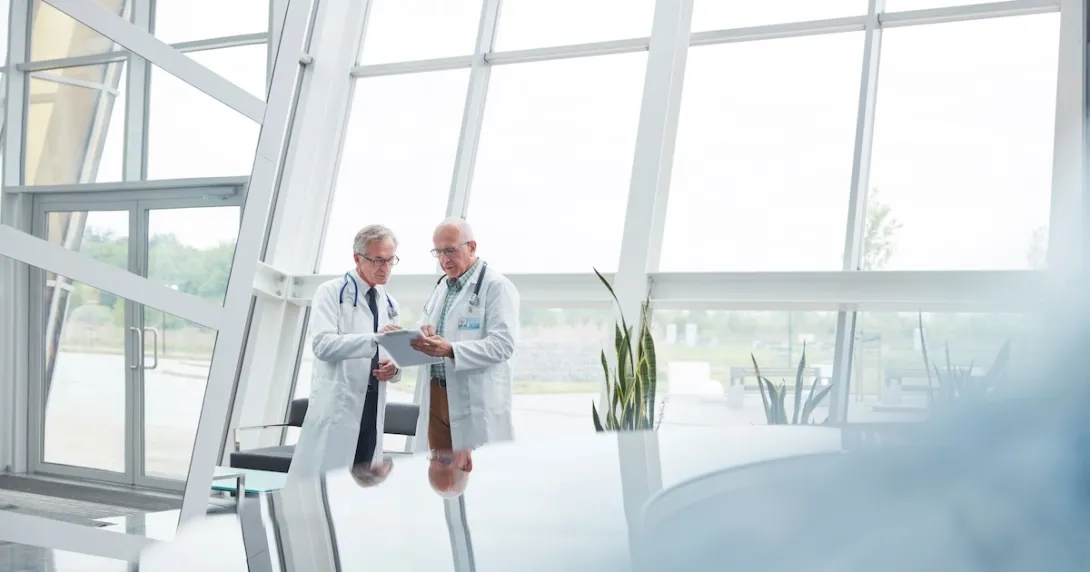 Two healthcare professionals standing in a large room with windows Two healthcare professionals standing in a large room with windows
