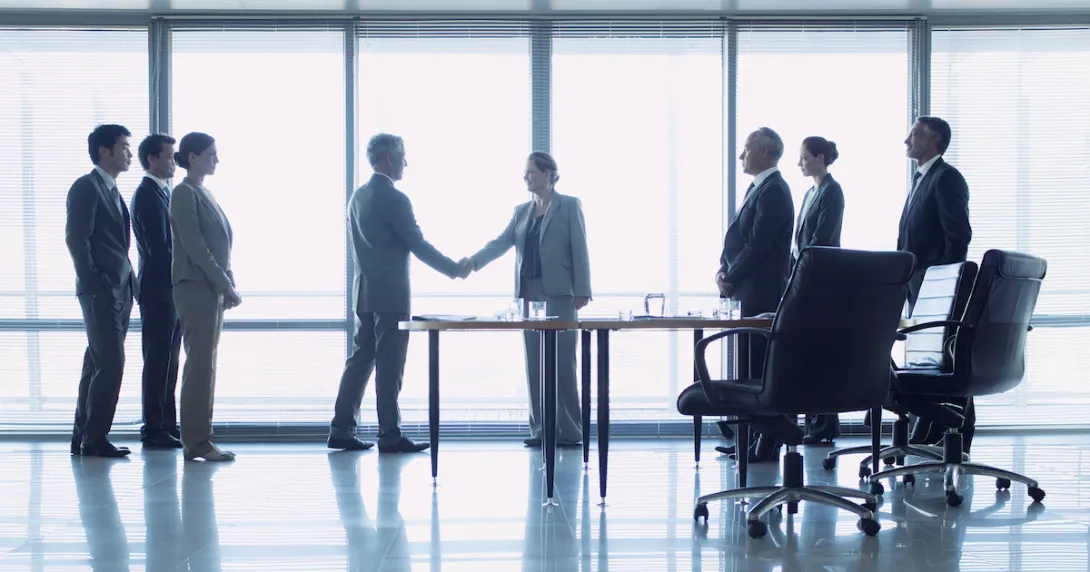 Two people shaking hands with six others watching