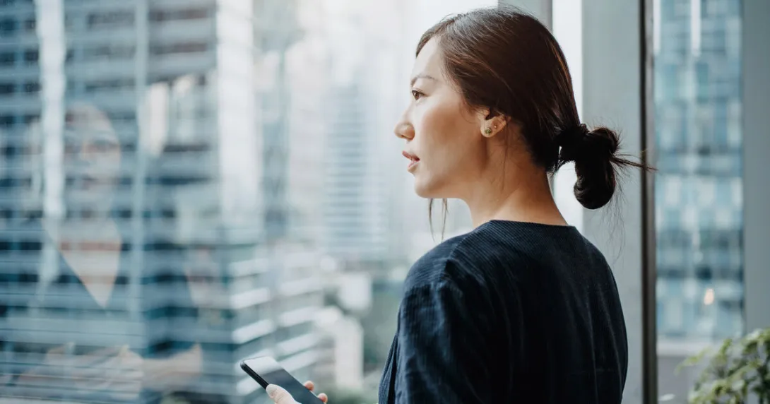 A person holding a smart phone looking out the window A person holding a smart phone looking out the window