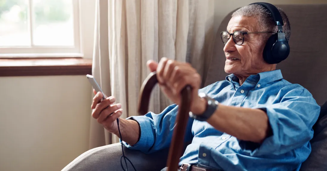 An older man with a cane using a smartphone in his home.